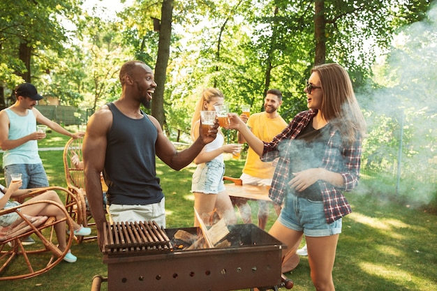 Free photo group of happy friends having beer and barbecue party at sunny day. resting together outdoor in a forest glade or backyard