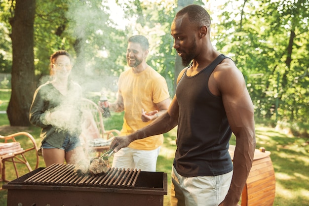 Free photo group of happy friends having beer and barbecue party at sunny day. resting together outdoor in a forest glade or backyard