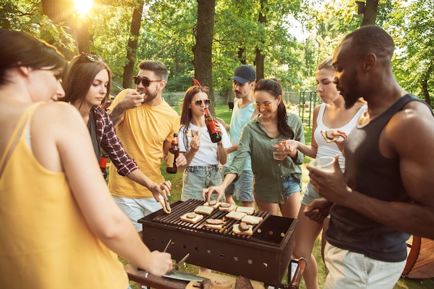 Free photo group of happy friends having beer and barbecue party at sunny day. resting together outdoor in a forest glade or backyard