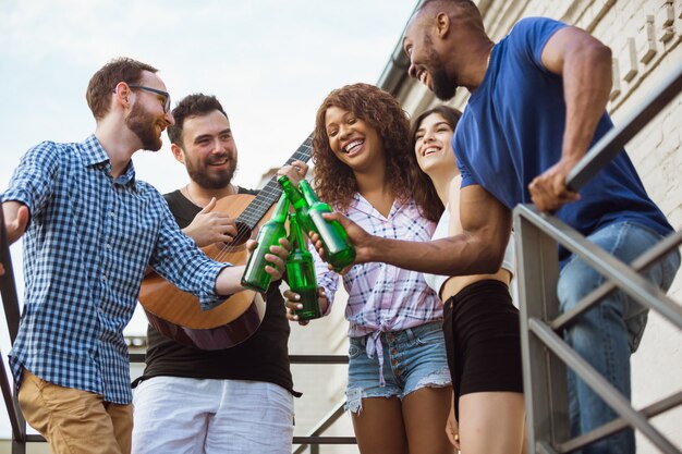 Group of happy friends having beer party in summer day. Resting together outdoor, celebrating and relaxing, laughting. Summer lifestyle, friendship concept.