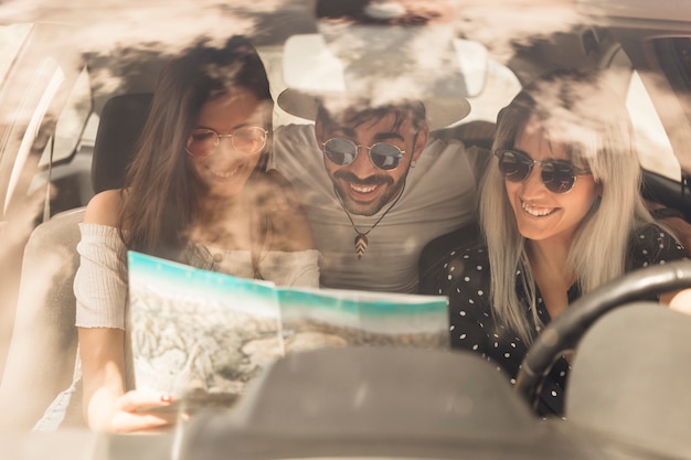 Group of happy friends looking at map sitting inside the car