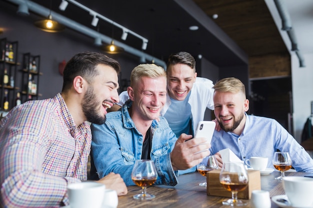 Free photo group of happy friends looking at smartphone sitting at restaurant