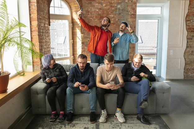 Free photo group of happy young caucasian people sitting on a sofa together.