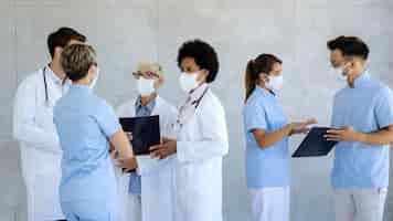 Free photo group of healthcare workers with protective face masks talking at hospital hallway