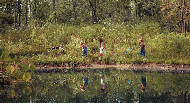 Group of kids walking through a field covered in greenery and reflecting on the lake under sunlight