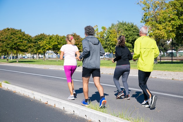 Group of mature joggers in sports clothes running outside, training for marathon, enjoying morning workout. Full length shot. Retired people and active lifestyle concept