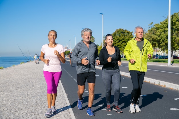 Group of mature people wearing sports clothes, jogging along river bank. Full length shot. Retirement or active lifestyle concept