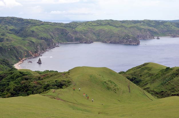 Group of people hiking the mountains around a sea surrounded by greenery under a blue sky