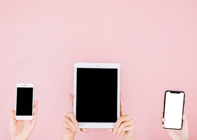 Group of people holding electronic gadgets on pink background