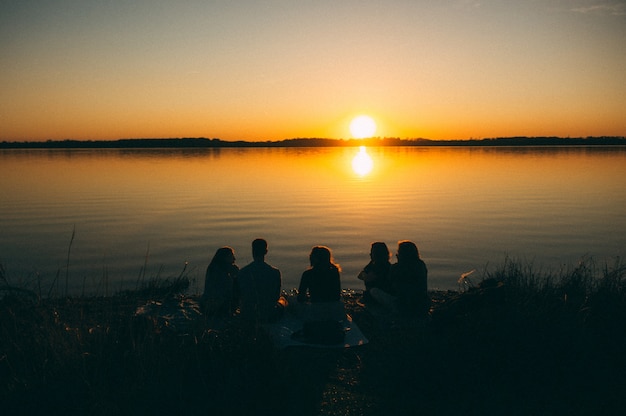 Group of people sitting by the sea enjoying the beautiful view of the sunset