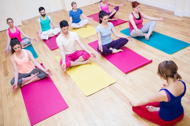 Group of people and trainer sitting in lotus position