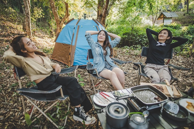 Free Photo group of pretty women sitting on camping chair at front of tent for relaxtion while has camping in nature forest with happiness together copy space