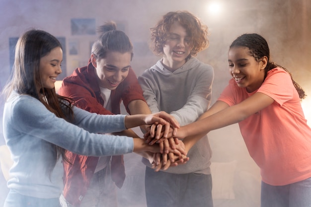 Group of teenage friends putting their hands together at home during party