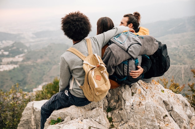 Free photo group of three friends sitting on top of mountain peak looking at view