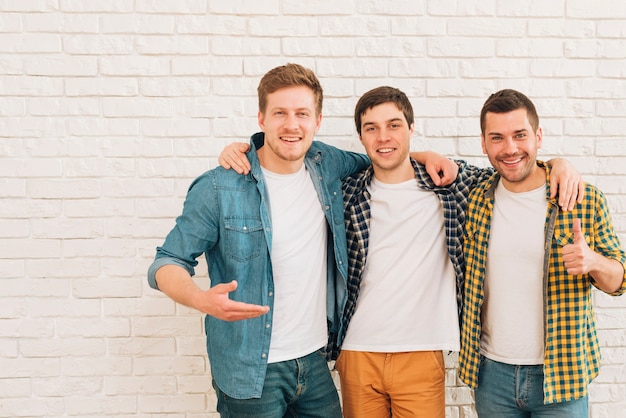 Group of three male friends standing together against white wall