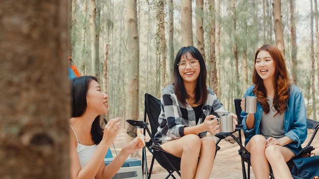 Group of young asia camper friends sitting in chairs by tent in forest