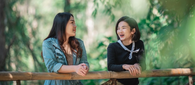 Group of young asian women standing on bamboo bridge are looking beautiful nature while camping in forest with happiness together