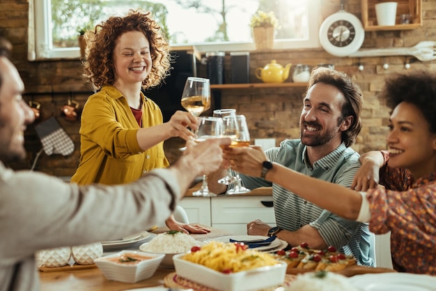 Group of young happy people having fun while toasting with wine during lunch at dining table