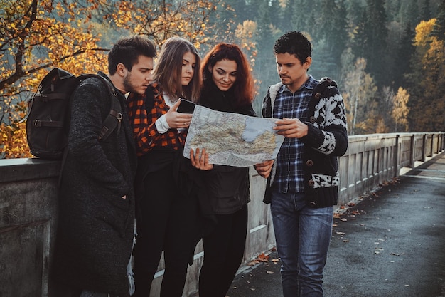 Group of young people are looking at the map where they are while walking in autumn forest.