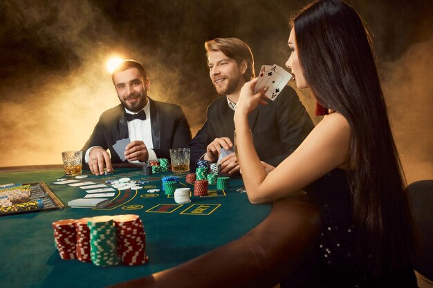 Group of young rich people is playing poker in the casino. Two men in business suits and a young woman in a black dress. Smoke. Casino. Poker