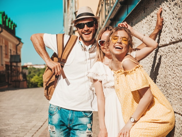 Free photo group of young three stylish friends posing in the street. fashion man and two cute girls dressed in casual summer clothes. smiling models having fun in sunglasses.cheerful women and guy outdoors