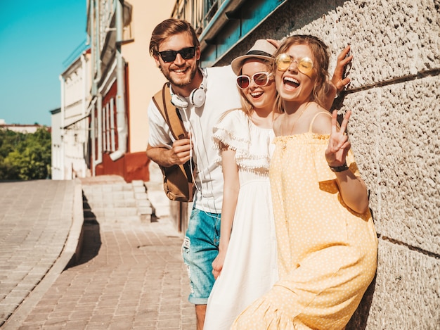 Free photo group of young three stylish friends posing in the street. fashion man and two cute girls dressed in casual summer clothes. smiling models having fun in sunglasses.cheerful women and guy outdoors