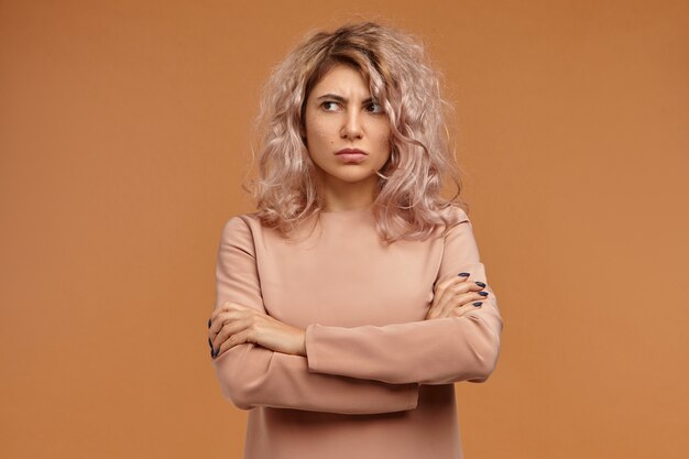 Grumpy stubborn hipster girl with voluminous hair expressing disrespect and indifference, not talking to you, looking away with displeased facial expression