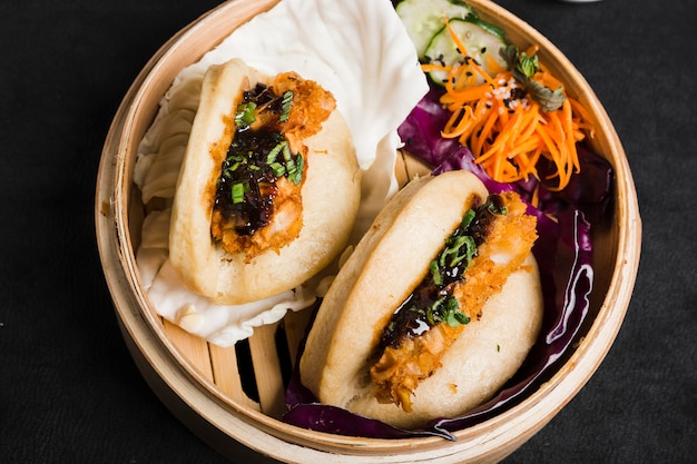 Free photo gua bao steamed buns with salad inside the bamboo steamer on black background