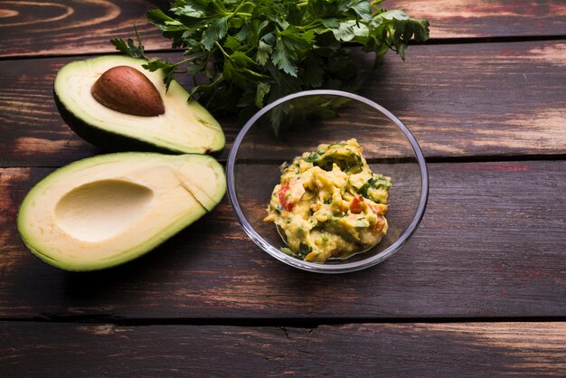 Guacamole in bowl and avocados near herbs