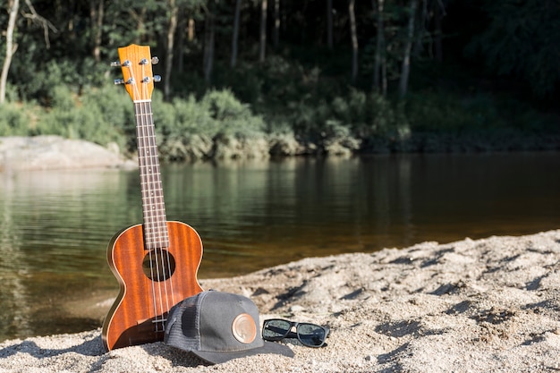 Free photo guitar with cap and sunglasses on shore near water