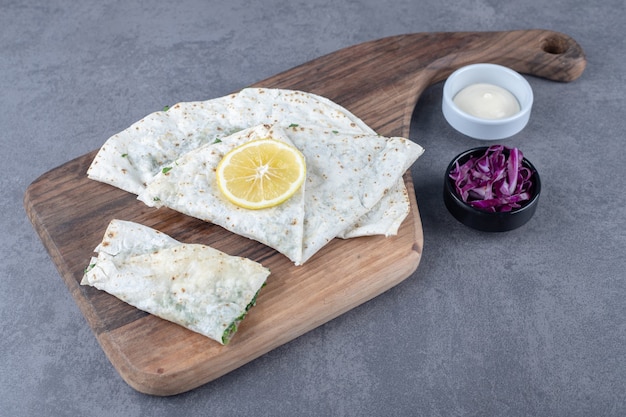 Gutab on the board next to a small bowl of grated red cabbage on the marble surface.