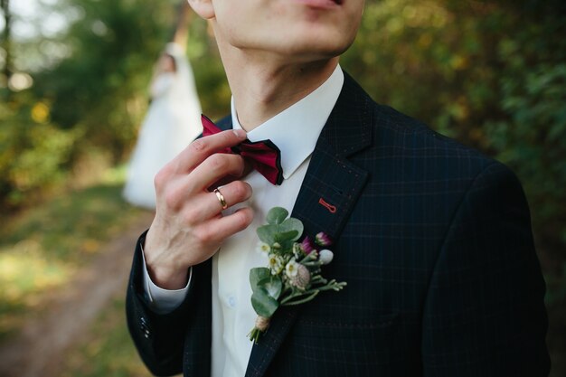 Guy adjusting bowtie standing in forest