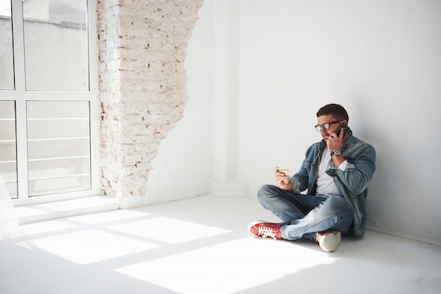 Free photo a guy in casual clothes is sitting at home in an empty apartment and calling on the phone.