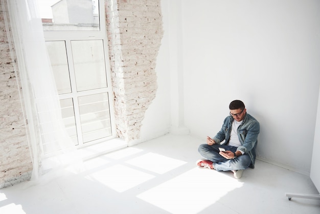 Free photo a guy in casual clothes is sitting at home in an empty apartment holding a credit card