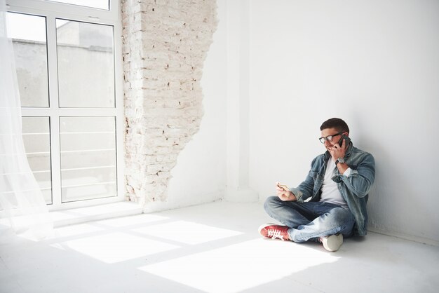 A guy in casual clothes is sitting at home in an empty apartment holding a credit card