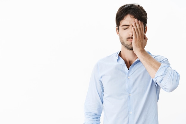 Guy feeling sad missing opportunity of lifetime being guilty and upset making facepalm gesture with hand on face standing with closed eyes feeling drained and uneasy after failure being fired