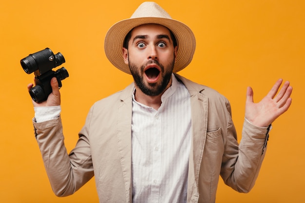 Guy in hat looks shocked into camera and holding binoculars