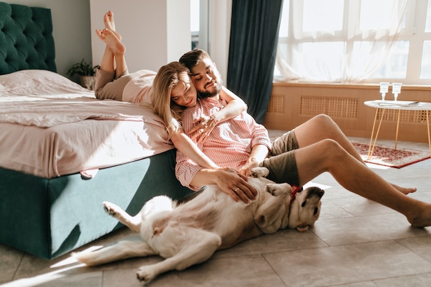 Free photo guy and his girlfriend are resting in bedroom. happy couple lovingly looking at their pet who wants to play.