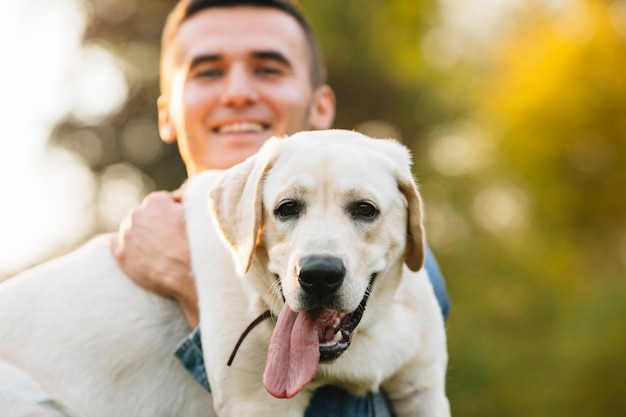 Guy holding his friend dog labrador and smiling at sunset