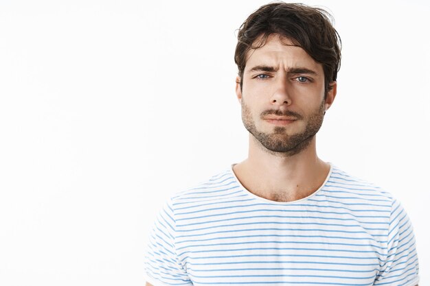 Guy looking frustrated and disappointed squinting feeling doubtful, unsure and suspicious standing confused against gray wall cannot get clue why wife acting strange over gray wall