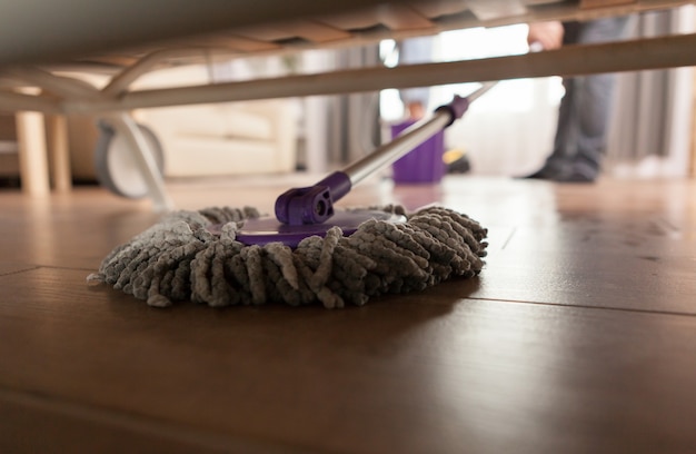 Free photo guy mopping the dust under sofa in apartment