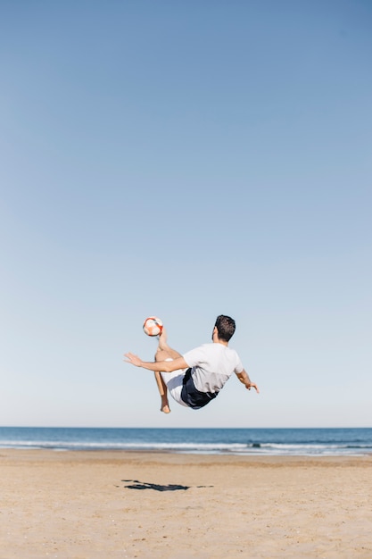 Free photo guy playing football at the beach