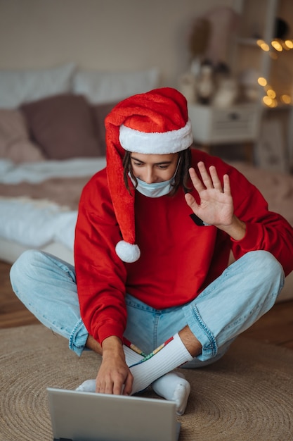 Free Photo guy in santa hat near the laptop is interacting through video calls. christmas in isolation at home. social distancing for holidays.