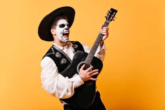 Free Photo guy singing emotional song plays guitar. portrait of man with painted face in sombrero,