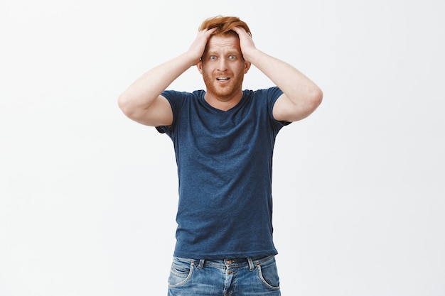 Free photo guy starts panicking. nervous and anxious attractive ginger man with beard, touching hair, staring shocked and worried