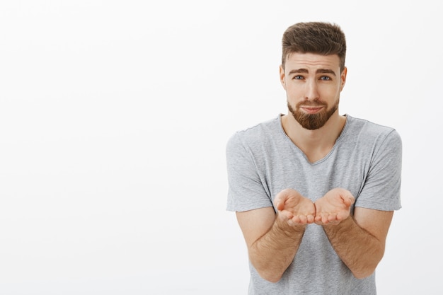 Free photo guy suggesting his heart being nice and cute boyfriend. charming handsome and masculine caucasian brunet holding palms near chest as if carrying something fragile in arms standing over gray wall