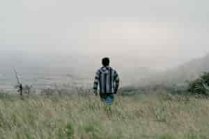 Free photo a guy walking in the field through grass on a gloomy foggy day