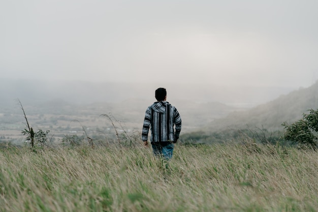 Free Photo a guy walking in the field through grass on a gloomy foggy day