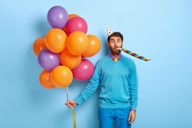 Free Photo guy with birthday hat and balloons posing in blue sweater