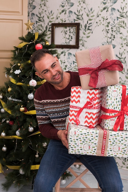 Guy with heap of gifts on chair near Christmas tree